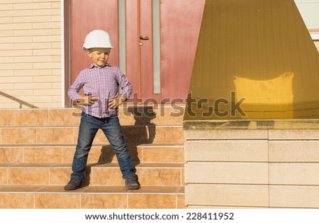 Confident Cute Little Kid in White Engineer Helmet Posing at the Outdoor House Stairs While Winking to the Camera.