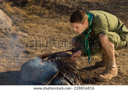 Young White Boy Scout Making Fire Out From Wood for Cooking at Campground.
