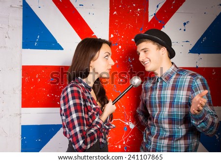 Close up Young Woman Interviewing Happy Handsome Young Man in Trendy Fashion Using Microphone, In Front British Flag Print.