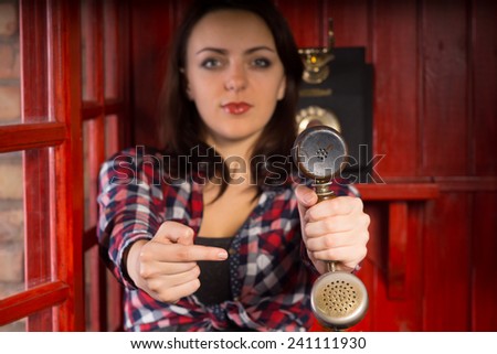 Attractive young woman pointing to a vintage telephone handset as she extends it towards the viewer in a helpful gesture indicating an incoming call