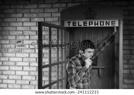 Young Man Calling Someone at the Telephone Booth with Brick Wall Background. Captured in Monochrome.