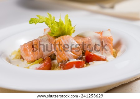 Grilled salmon seafood starter with small portions of fillet, drizzled with a creamy savory sauce and served with lettuce and tomato