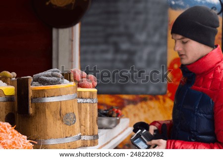 Young man dressed in warm winter clothing opening his wallet and making a purchase at an outdoor stall