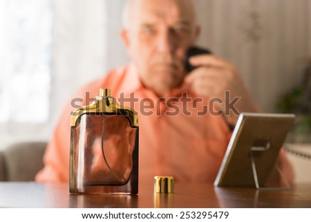 Close up Open Aftershave Bottle on a Table In front Old Man Shaving his Beard with Razor and Small Mirror.