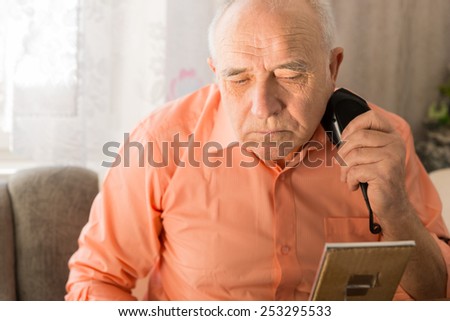 Close up Serious Old Man Shaving Beard with Electric Razors While Facing Small Mirror on the Table.