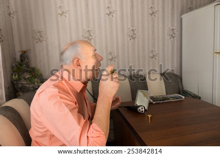 Close up Side View of Old Bald Man Spraying Aftershave on his Face After Cleaning his Beard While Sitting at the Sofa Inside the House.