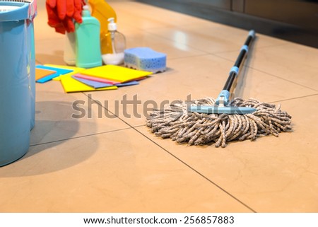 Household string mop and bucket for cleaning the floors with various cleaning supplies in the background