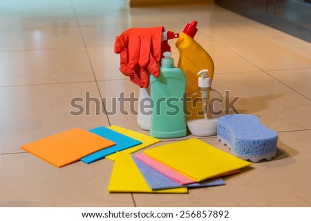 A display of a variety of household cleaning products on a tiled floor including new absorbent cloths, a sponge, gloves and various containers, with copyspace