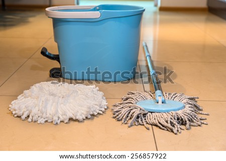 Old wet mop with a new replacement head and bucket on a tiled floor in a kitchen or bathroom in a household chores and hygiene concept