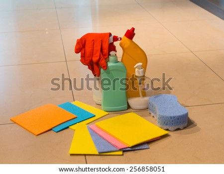 Assorted colorful cleaning products displayed on a tiled floor including absorbent cloths, rubber gloves, sponge and plastic containers for disinfectants