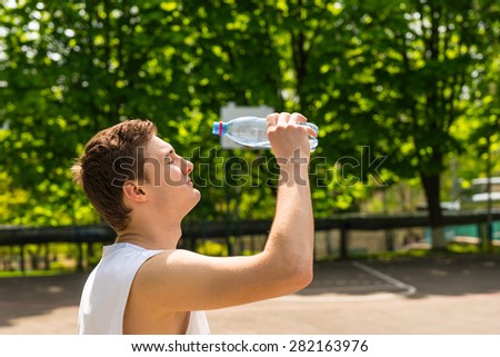 Head and Shoulders View of Young Athletic Man About to Pour Water from Bottle onto Face, Taking a Break for Refreshment and Hydration on Basketball Court