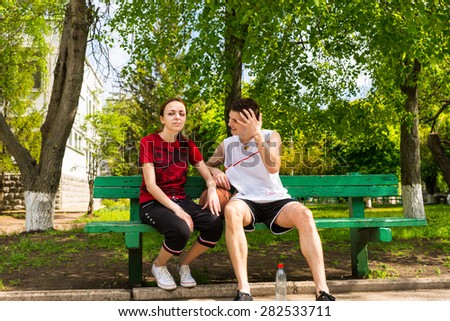 Portrait of Young Man and Woman Wearing Athletic Clothing Sitting on Green Park Bench with Basketball Between Them, Taking a Break After the Game