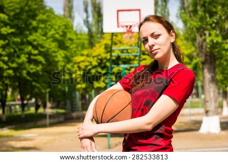 Portrait of Serious and Confident Young Woman Wearing Red T-Shirt Holding Basketball on Outdoor Court