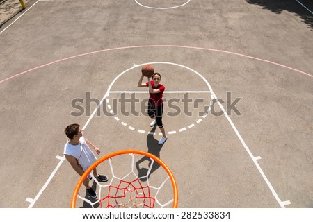 High Angle View from Backboard of Young Athletic Woman Taking Shot on Net While Man Watches on Outdoor Basketball Court
