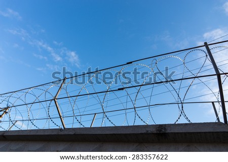 Razor Wire Along Top of Security Fence at Prison or Other High Security Facility with Sunny Blue Sky in Background