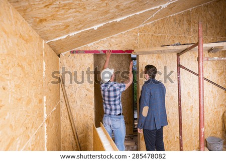 Builder and Architect Inspecting Construction of Door Frame with Level Inside Unfinished Home with Exposed Particle Plywood Boards