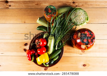 Bottling fresh vegetables for storage with assorted fresh veggies on a wooden table with two glass jarsof homemade preserves in a country lifestyle concept