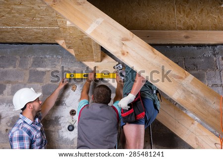 Team of Construction Workers Building Wooden Staircase Frame in Unfinished Basement of New Home, Checking Levels for Accuracy and Quality Control