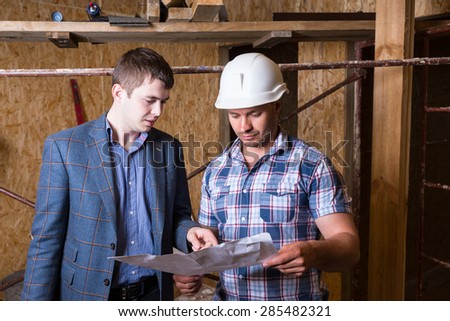 Architect and Construction Worker Foreman Inspecting Plans Together Inside Unfinished Building