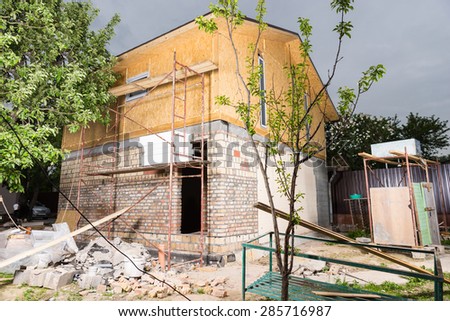 Exterior of Partially Finished New Home, Scaffolding and Building Supplies Stacked Outside Unfinished Home on Construction Site