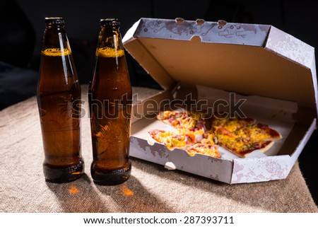 Side View of Bottles of Beer on Burlap Covered Table Beside Cardboard Take Out Box of Pizza with Open Lid