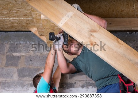 Two Men Working Together to Build Wooden Frame for Stairs with Power Tools, Leading into Basement of Unfinished Home