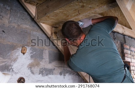 Male Construction Worker Builder with Cordless Drill Building Frame for Stairs in Basement of Unfinished Home with Exposed Cement Wall