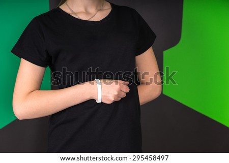 Mid section front view of young female wearing black t-shirt and white wristband, hand in a fist against abdomen, other hand behind back on a green and black background.