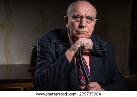 Close up Serious Middle Aged Bald Businessman in Formal Attire, Holding his Cane and Looking at the Camera While Leaning his Chin on his Hand.