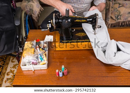 High Angle View of Unidentifiable Man Mending Pants Using Old Fashioned Manual Sewing Machine on Table Surrounded by Sewing Supplies