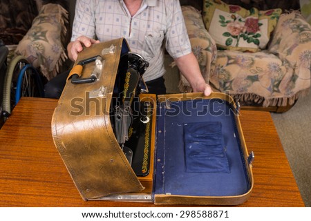 Tailor Man Keeping his Sewing Machine in a Vintage Case On top of a Wooden Table In the Living Room.