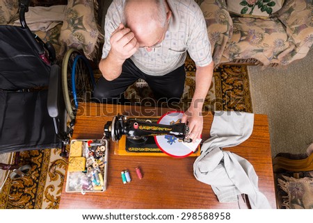 High Angle View of Senior Man Working on Needle Point Wall Hanging Craft Using Old Fashioned Manual Sewing Machine at Home in Living Room