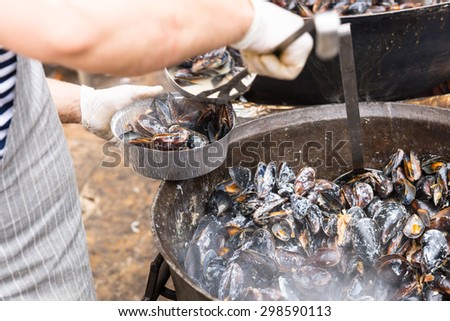 Close Up of Person Serving Single Portion of Hot Steaming Mussels from Large Pot into Take Out Container