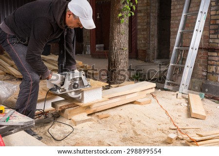 Man Using Handheld Power Saw to Cut Planks of Wood Leaving Behind Piles of Saw Dust on Floor