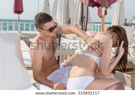 Gentleman Helping his Girlfriend in Applying Lotion for Sun Protection on her Back While Sitting on the Lounge Chair in the Resort.