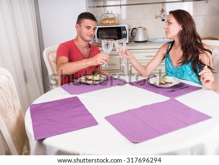 Young Couple Toasting with Glasses Water Before Eating Home Cooked Meal at Dinner Time While Seated at Dining Table in Small Kitchen