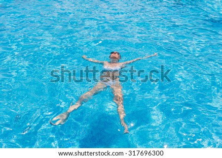 High Angle View of Relaxed Young Woman Wearing White Bikini Floating on Back in Clear Water of Resort Swimming Pool on Sunny Day