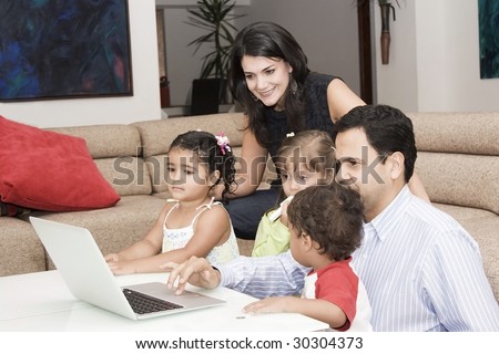 Portrait of family, mom, dad and their children enjoying indoor with a laptop