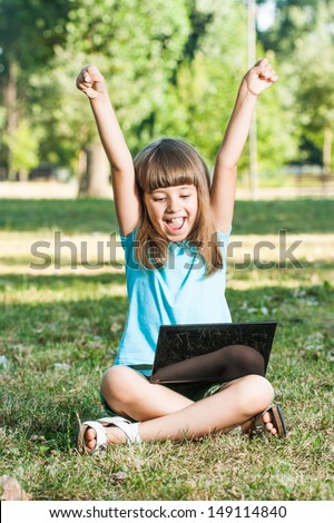 Little girl is sitting in park and she is excited because of something she saw on her laptop,Excited little girl with laptop