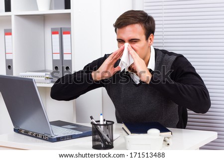 Businessman sneezing while working in his office,Businessman having flu