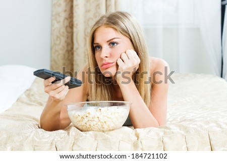 Blonde woman is feeling lazy,she is trying to find something interesting on tv to pay her attention,but there is nothing interesting,I\'m so bored!