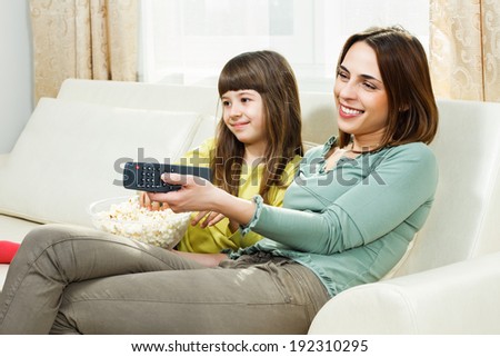 Mother and daughter sitting on sofa at their home,eating popcorn and watching tv,Family time