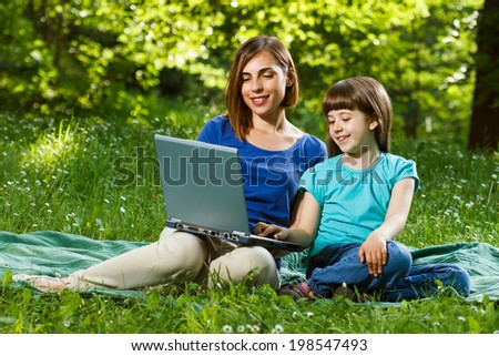 Mother and daughter using laptop while sitting in the beautiful nature,Mother and daughter using laptop