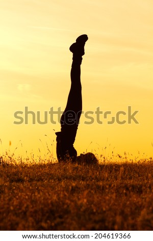 A silhouette of a woman practicing yoga, Niralamba Sarvangasana, with hands behind back. Unsupported shoulder stand.