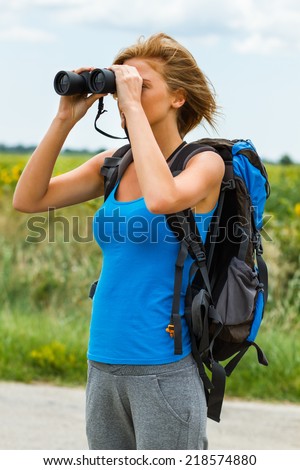 Woman is standing on the country road and  watching something through binoculars,Enjoying in nature with binoculars