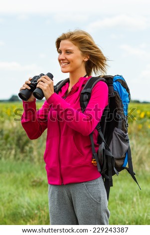 Cheerful blonde woman is standing in the nature and holding binoculars,Enjoying nature with binoculars