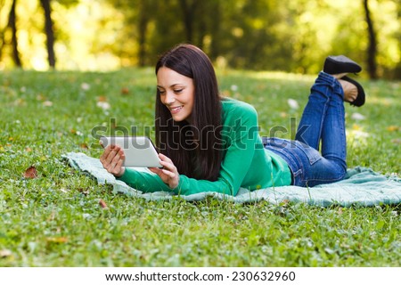 Young woman is using her digital tablet while lying down in the nature,Woman using digital tablet