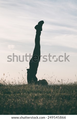 A silhouette of a woman practicing yoga,intentionally toned image.Yoga-Niralamba Sarvangasana with hands behind back/Unsupported shoulderstand