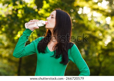 Beautiful woman is standing in the park and drinking water.Refreshment