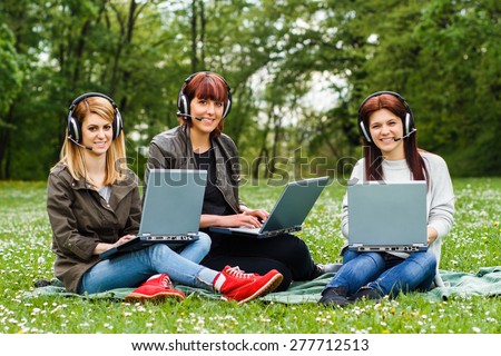 Four young girls sitting in the park and using laptop.Happy girls using laptop
